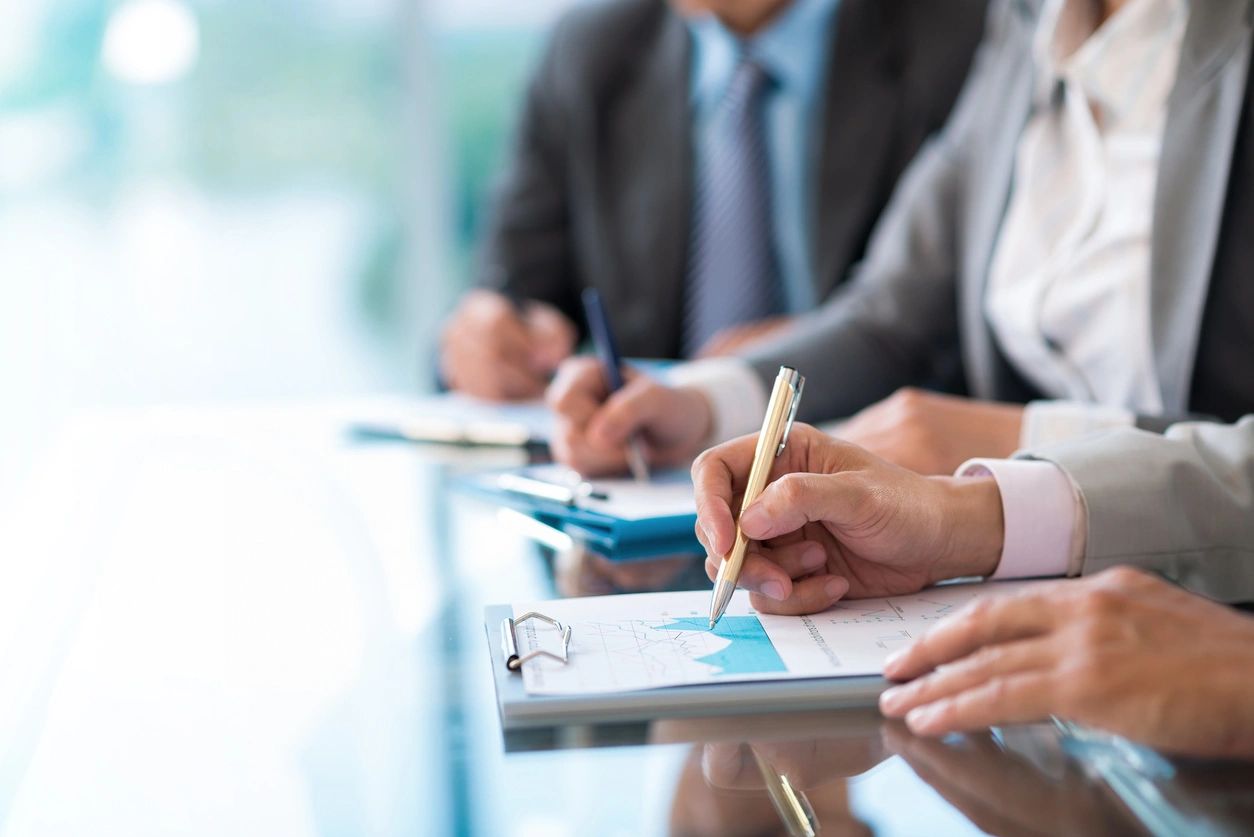 A group of people sitting at a table with pens and paper.