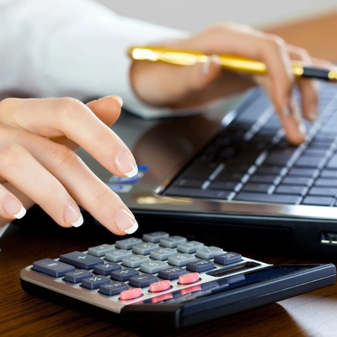 A person using a laptop and calculator on a desk.